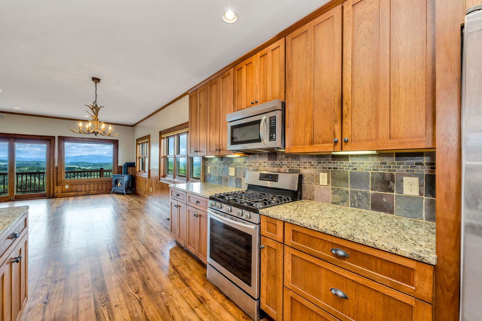 Luxury kitchen that features a gas range, stainless steel appliances, custom cabinetry, granite counter tops, and natural stone backsplash