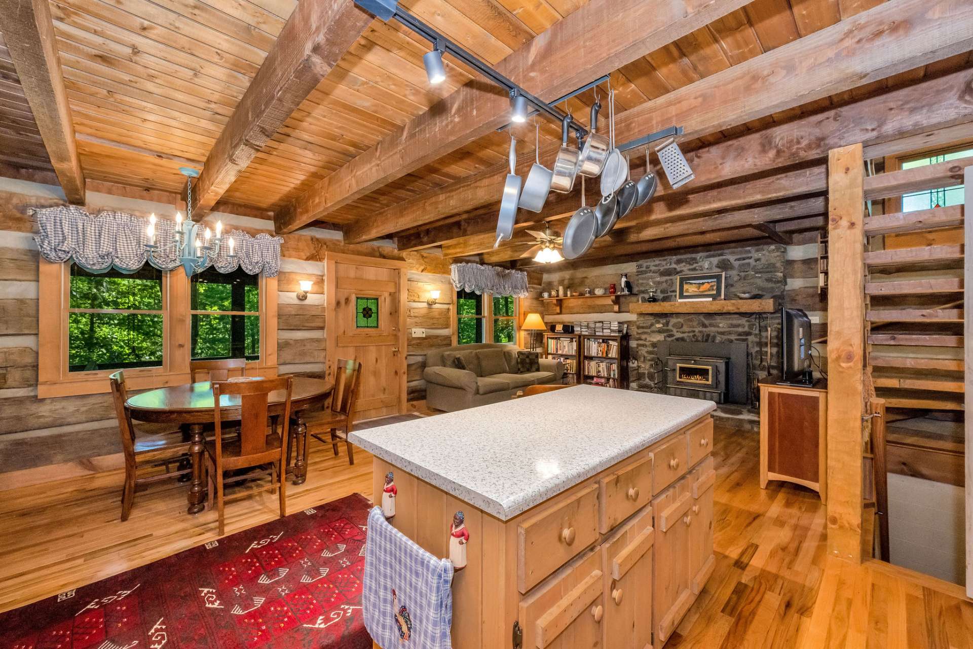 The kitchen, dining, and living areas blend effortlessly beneath rustic beamed ceilings, and the native stone fireplace anchors the room with elemental character.