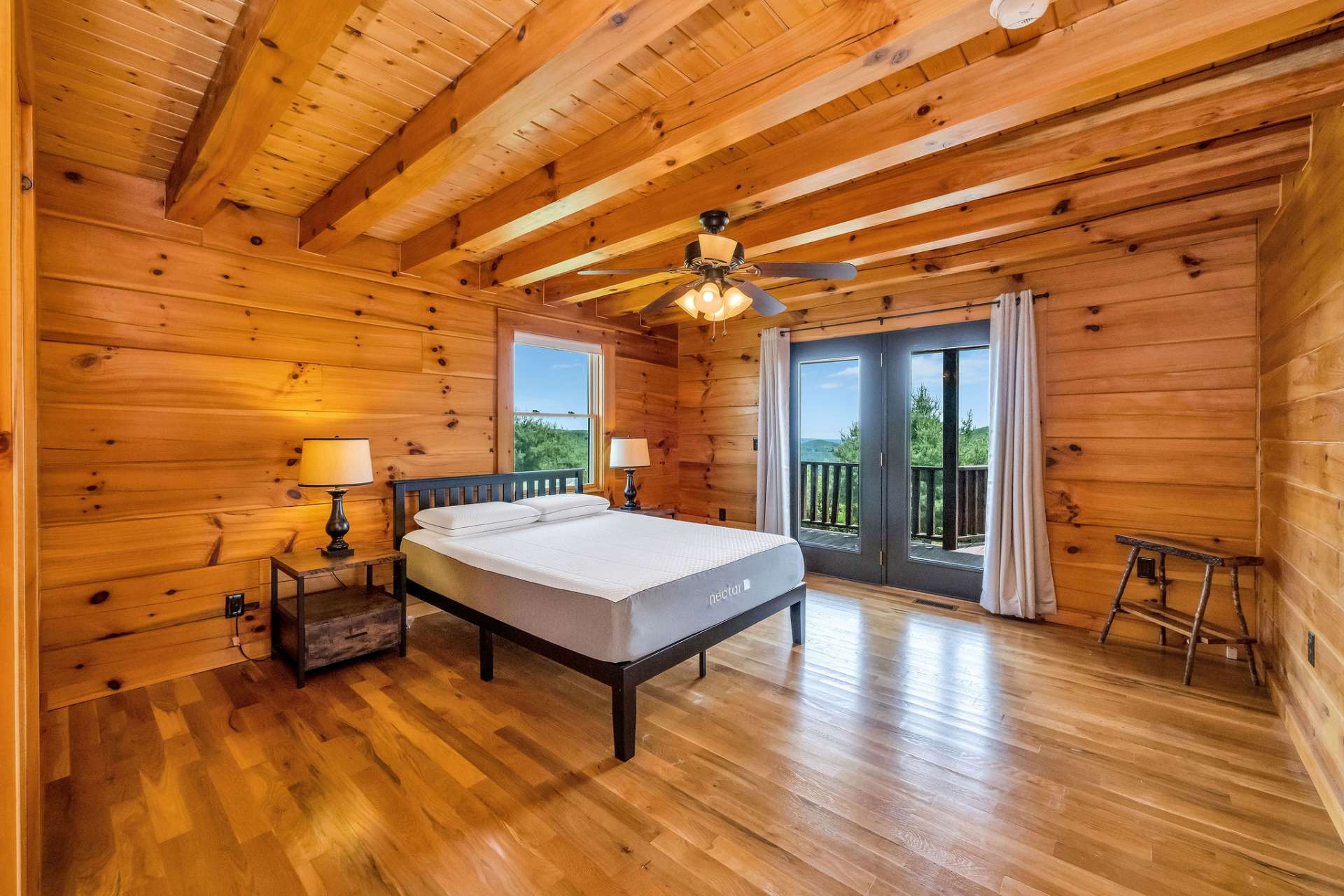 The spacious primary suite features a continuation of the gleaming hardwood flooring and tongue-and-groove ceiling with exposed beams. It also includes access to the rear deck.