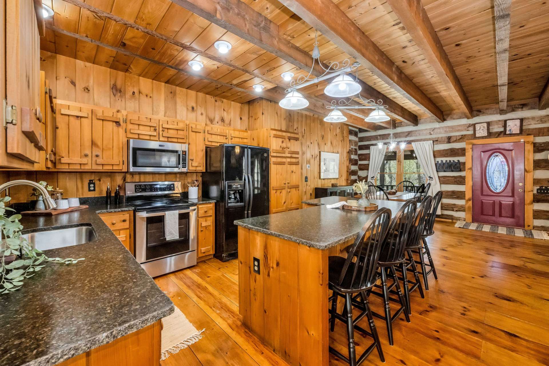 Striking black leathered granite countertops with a natural rough edge bring a chic, organic elegance to the kitchen, beautifully enhanced by black and stainless appliances, black bar seating, and the warmth of rich wood tones.