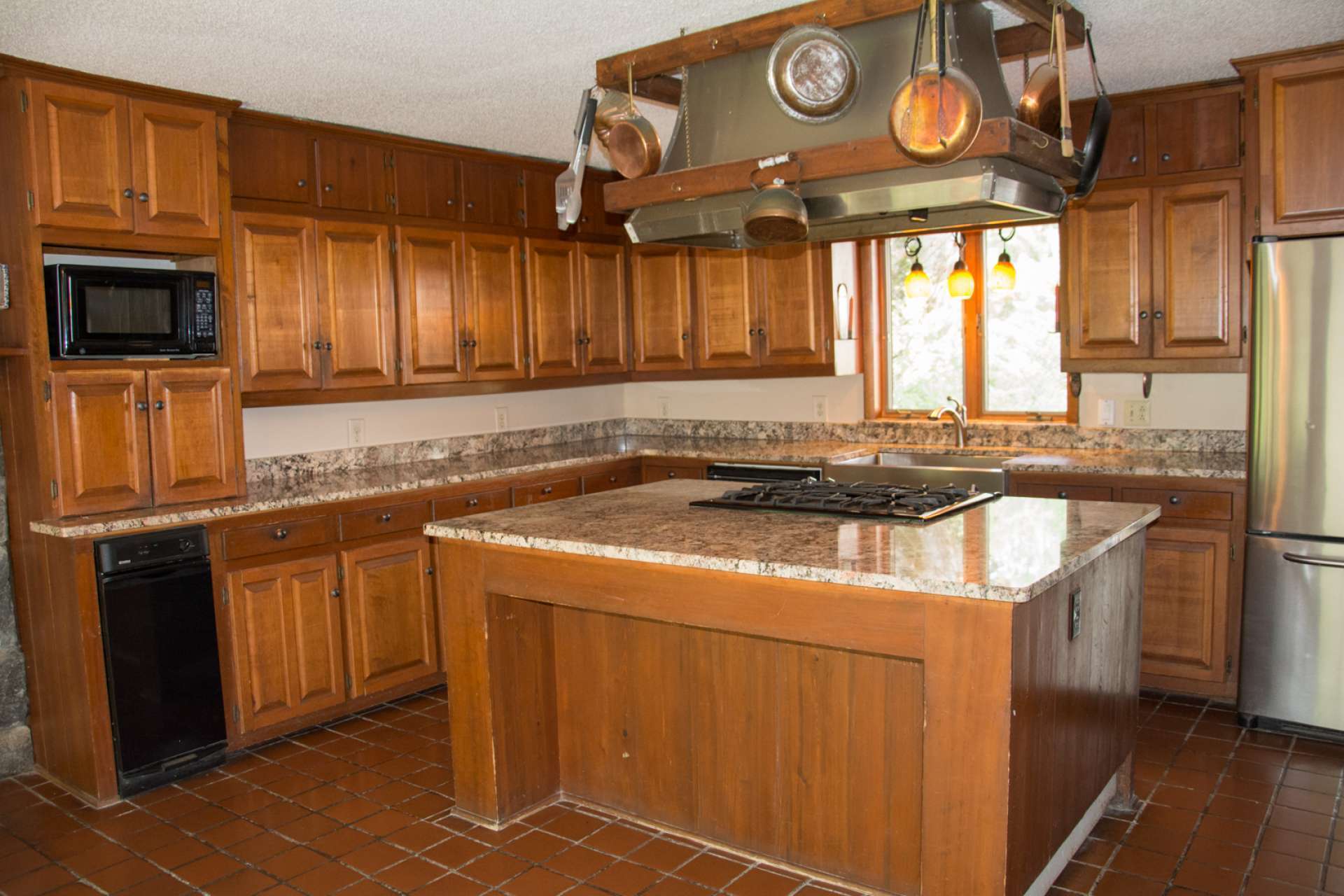 A spacious kitchen with granite counter tops, apron sink, large center island, gas range, and tiled floor.