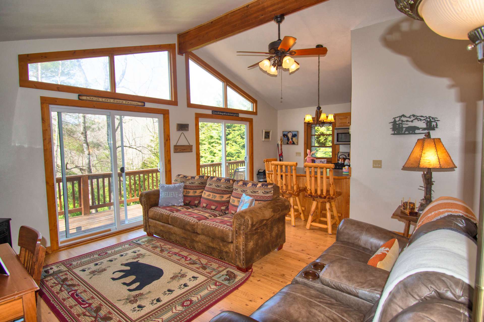 A one-level living floor plan includes a great room with slightly vaulted ceiling, gas stove, two sliding glass doors and high windows filling the room with natural light and a view of the surrounding forest.