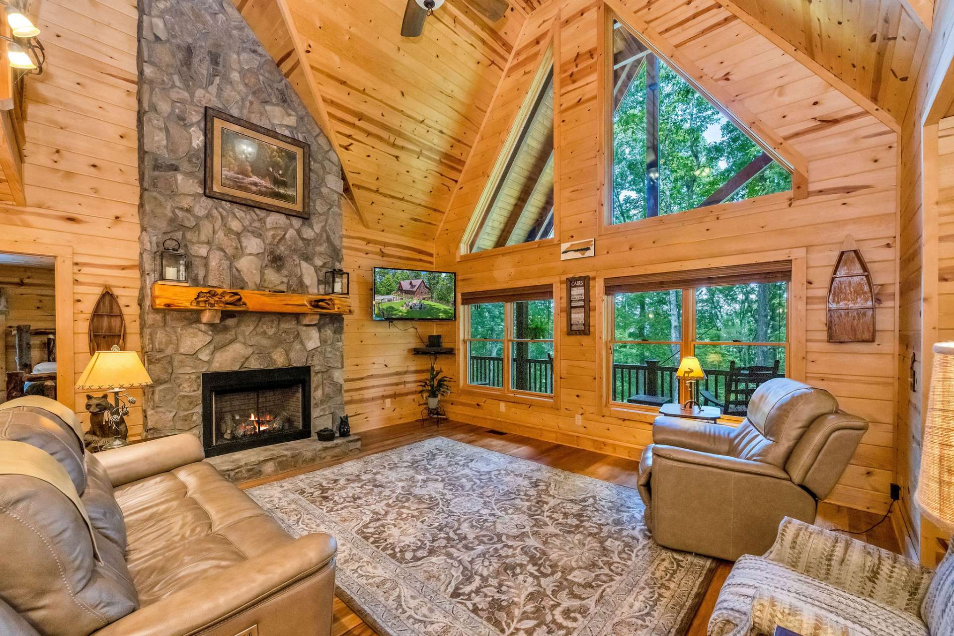 The great room impresses with vaulted wood ceilings, picture windows that frame the outdoors, and a two-story stone fireplace crowned by a hand-carved mantel.