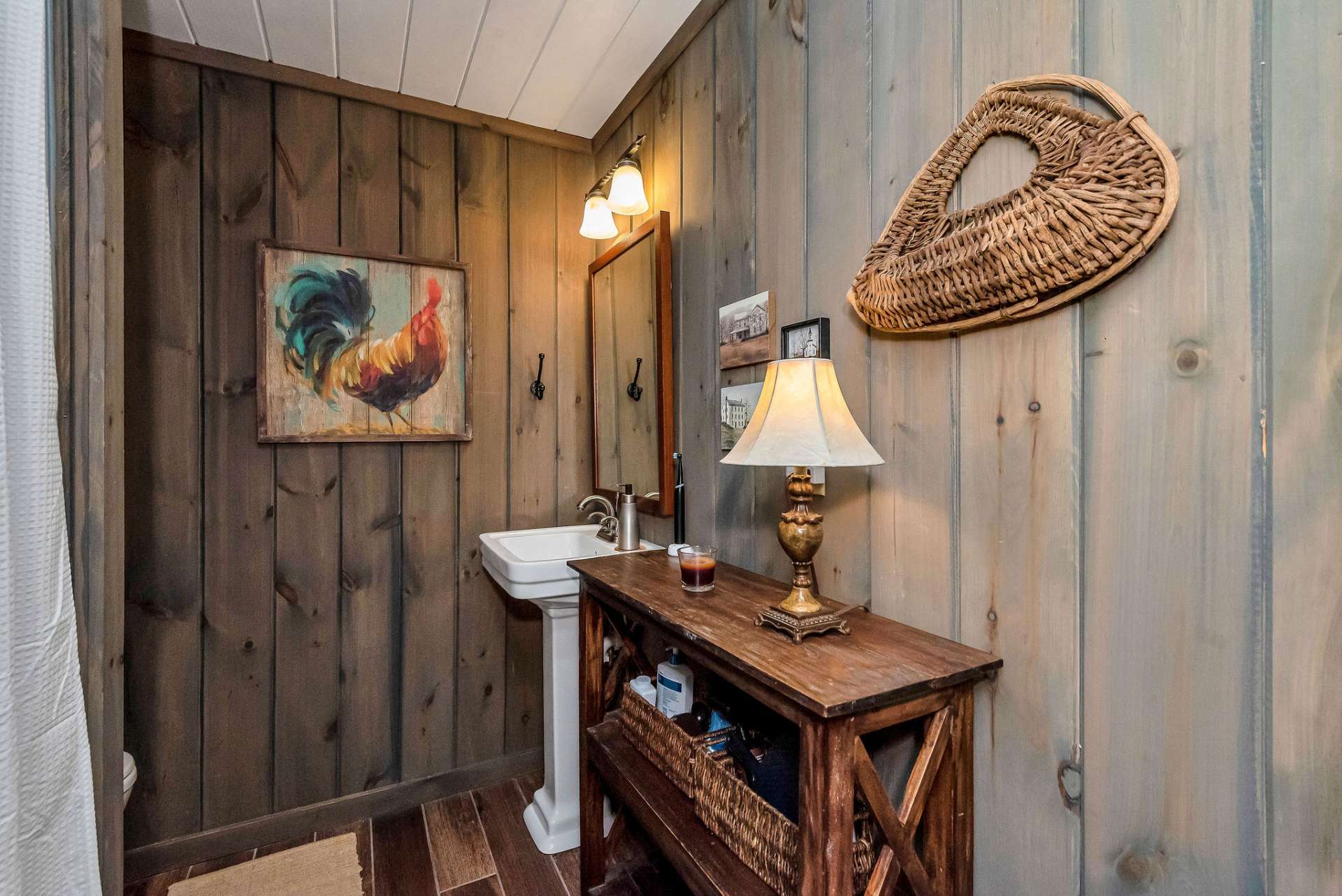 The lower level bathroom complements the cabin's overall rustic vibe and features a shower with a seat, a pedestal sink and a rustic piece of furniture which provides both storage and character.