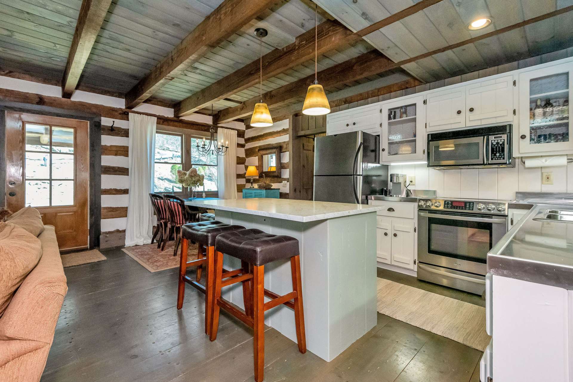 At the center of the kitchen stands a spacious island, topped with light marble that adds an elegant touch to the rustic setting. It not only provides additional workspace for meal preparation but also bar seating and extra storage beneath.