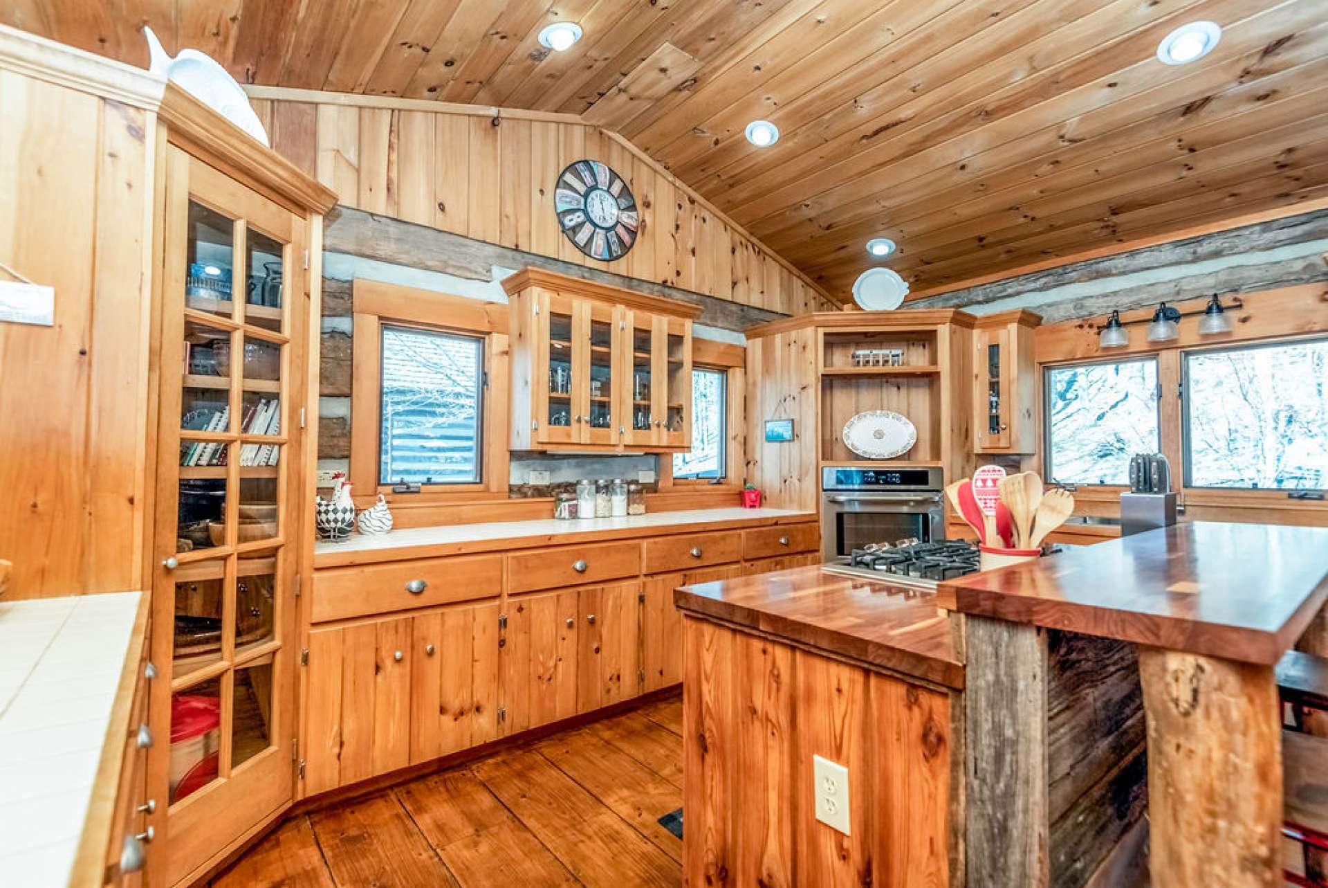 Island's countertops are a beautiful shiny wood and the bar is contrasted with reclaimed barn wood. This piece intertwines rustic and sleek for a style all it's own. Custom cabinetry and corner pantry provide ample storage for dishes, cookware and canned goods.