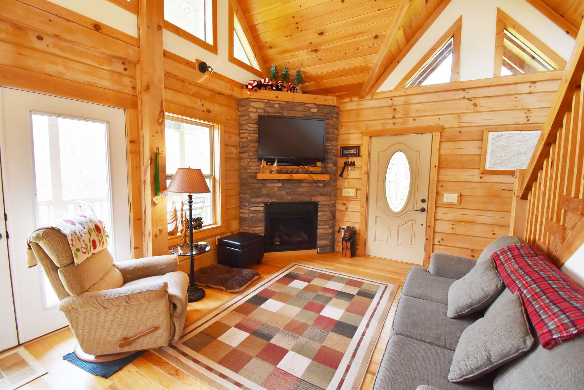 The bright and sunny vaulted great room features a wall of windows  filling the space with natural light, gleaming hardwood floors, and a stone fireplace with gas logs for added warmth and fireside romance on chilly winter evenings.