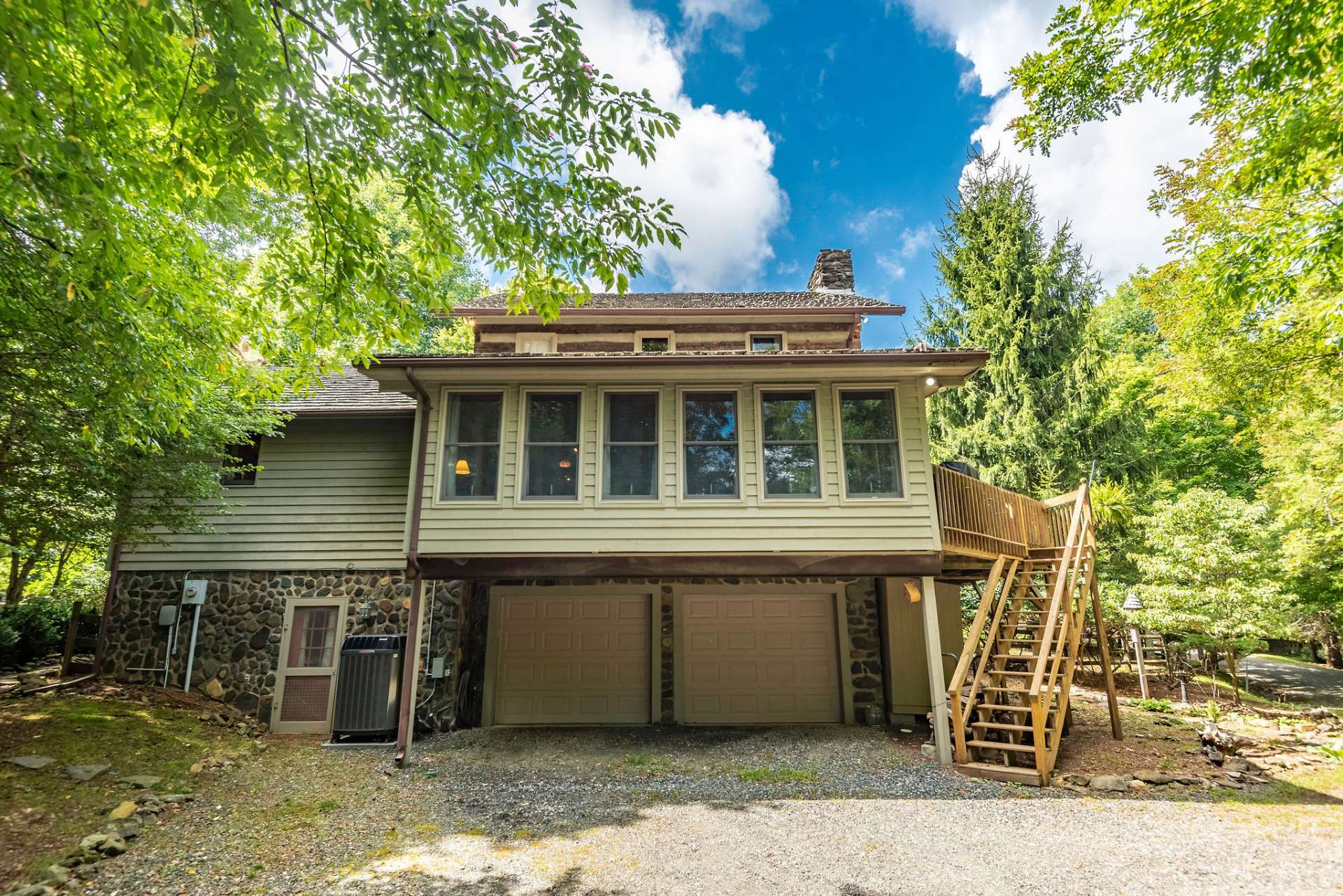 View of the back of cabin with a rear driveway to two car garage and stairs leading to side deck. A handy storage shed is tucked underneath deck for your garden tools.