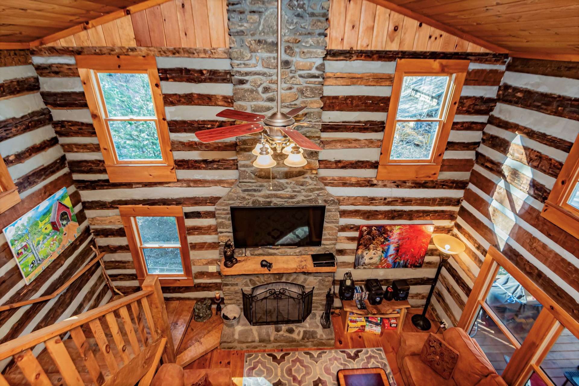 View from the loft down to the great room showcases the stone fireplace as well as abundant lighting from the many windows.